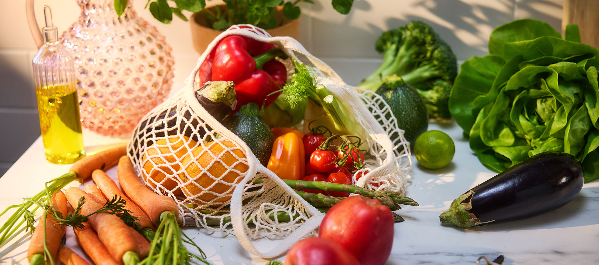 Fresh vegetables and fruits including carrots, bell peppers, tomatoes, lettuce, and eggplant on a table.
