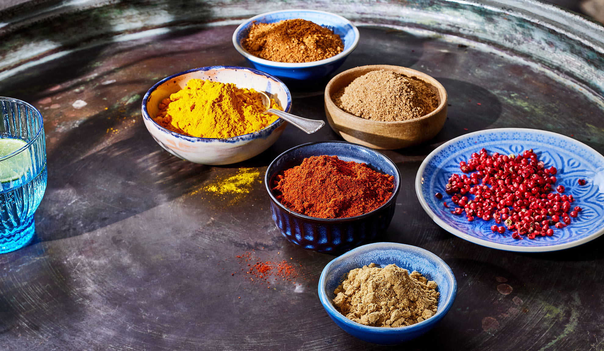 Various spices in bowls: turmeric, paprika, pepper, and others on a metal tray.
