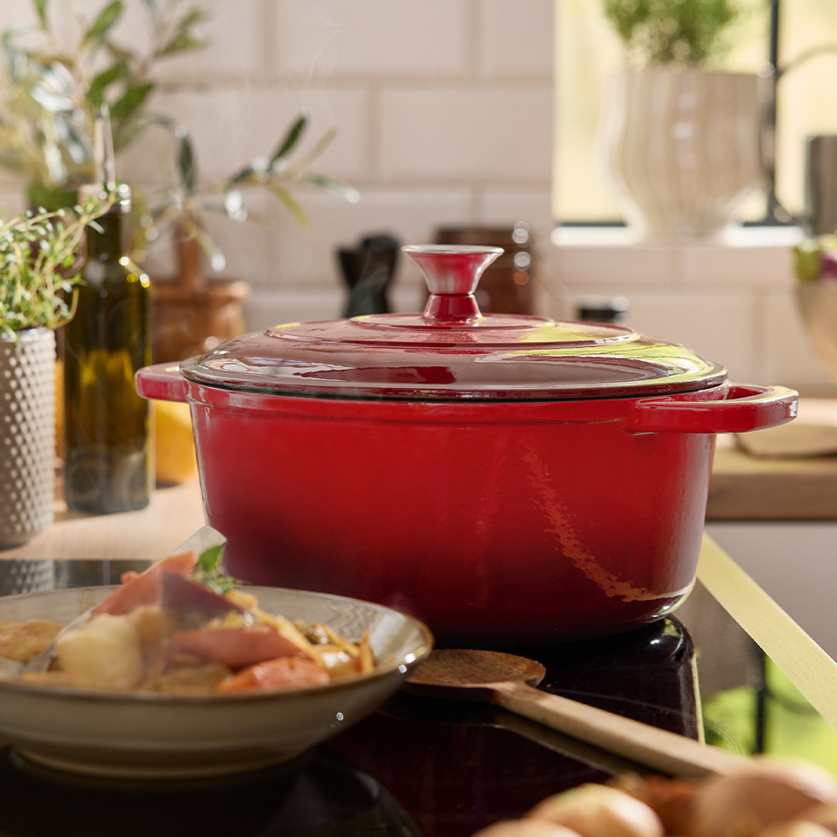 A red cast iron pot on a stovetop, with a bowl of cooked food alongside.