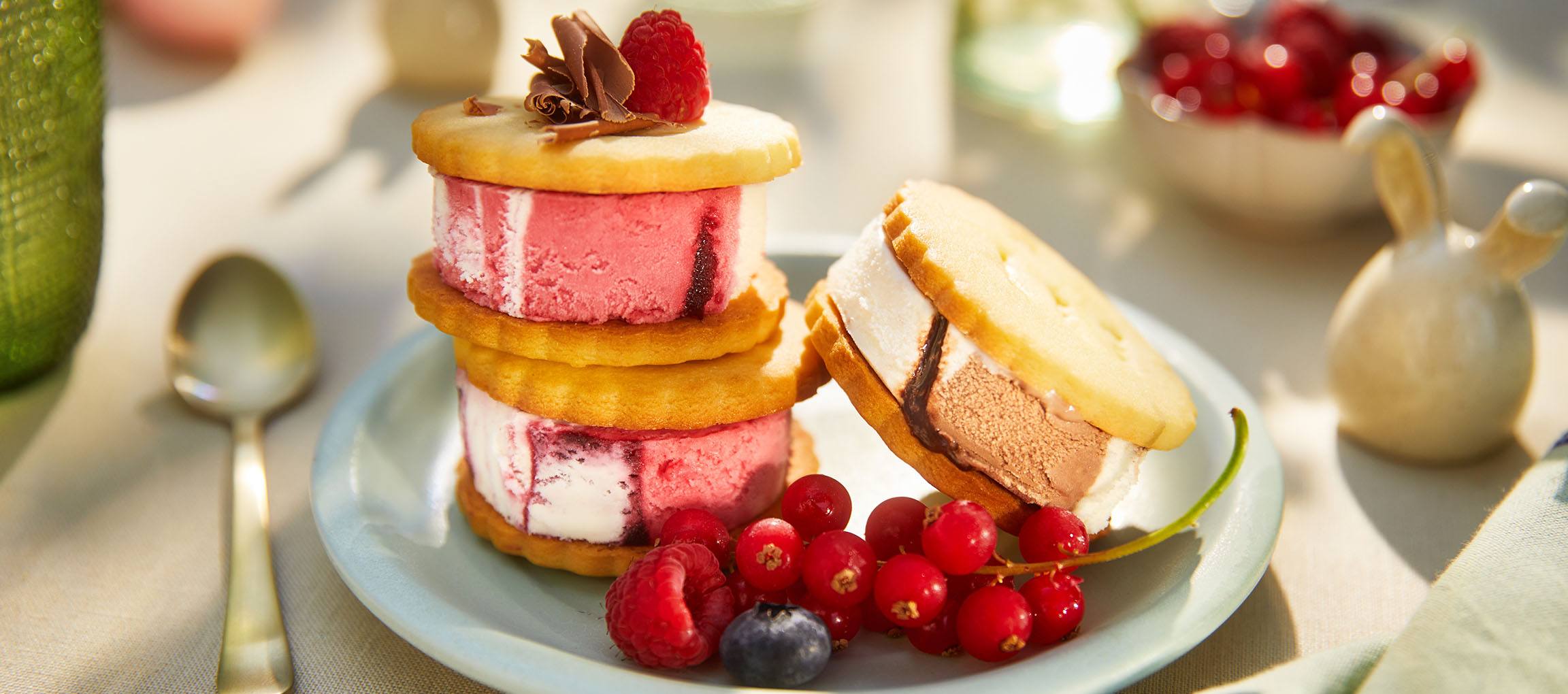 Ice cream sandwiches with berries on a light blue plate in a sunny outdoor setting.