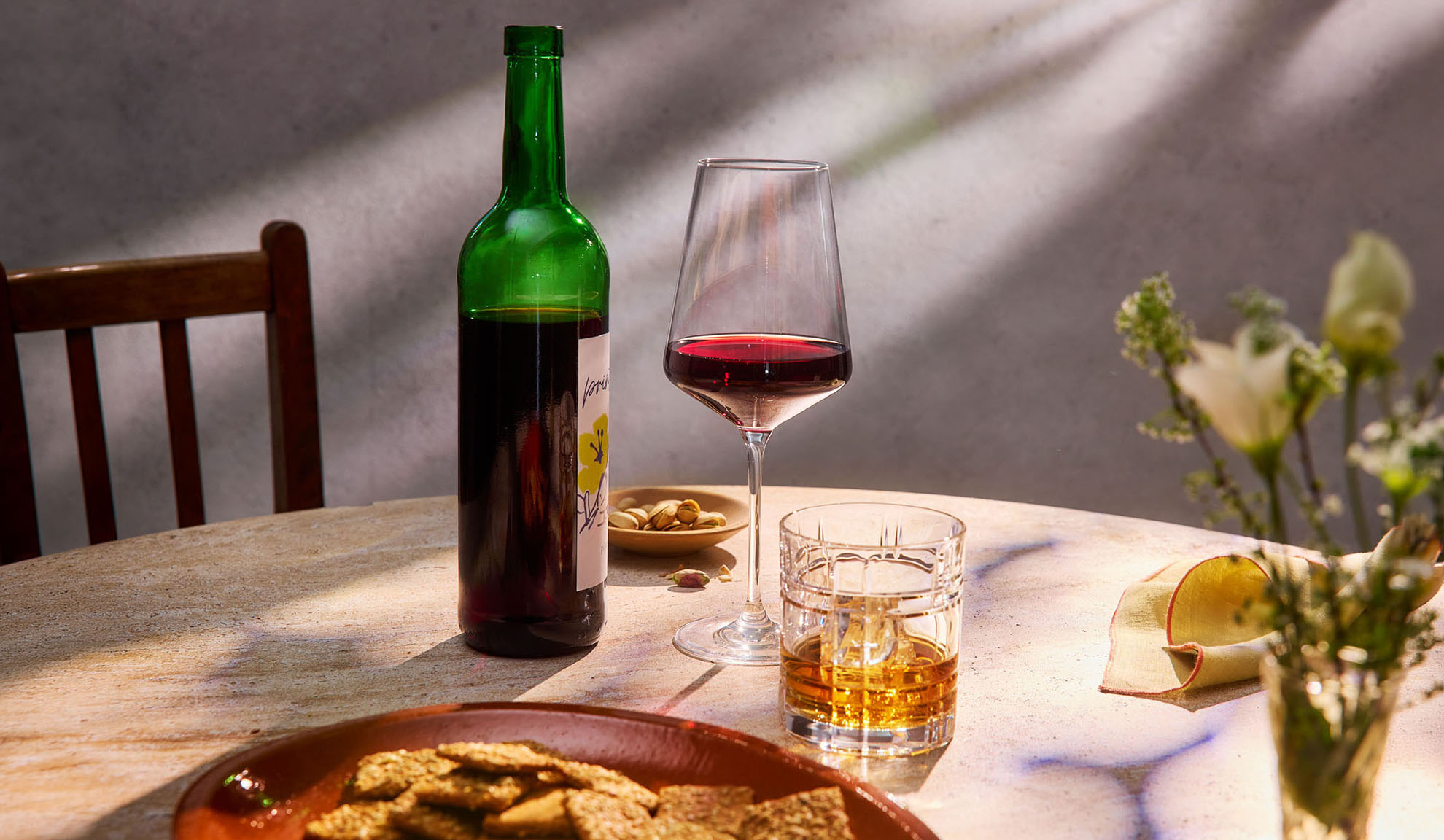 Red wine, whiskey, and snacks on a table in sunlight.