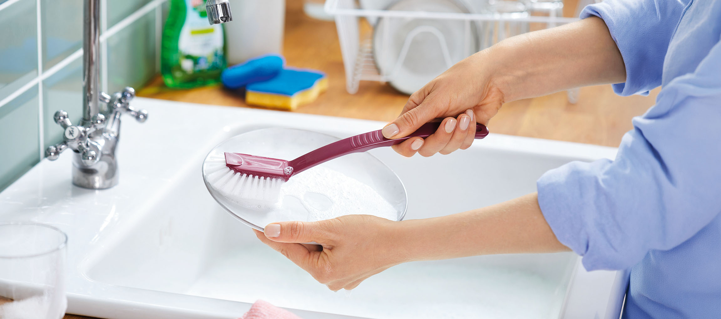 Woman washing dishes in a sink with a dish brush and a plate.