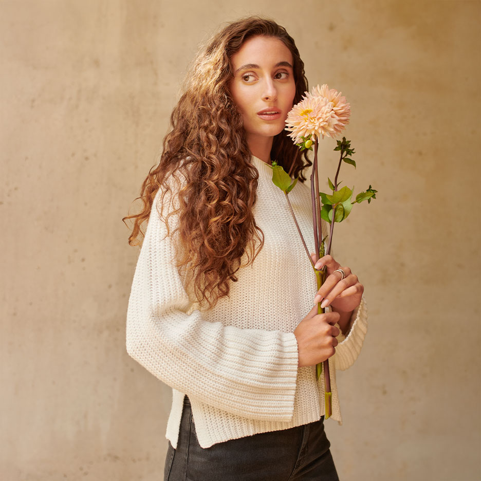 Woman with curly hair and white sweater, holding peach-colored dahlias.