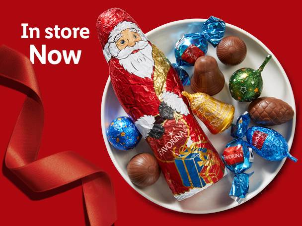 A chocolate Santa, bells, and other holiday-themed chocolates on a white plate with a red ribbon.