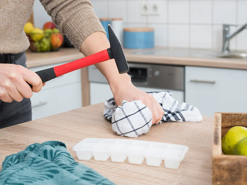 Woman using a hammer and ice cube tray in the kitchen.
