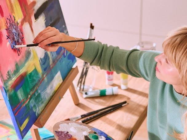 Child painting on an easel with acrylic paints and brushes.