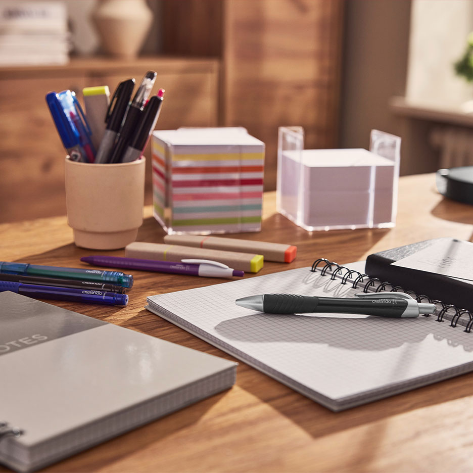Desk with notebooks, pens, highlighters, and sticky notes.