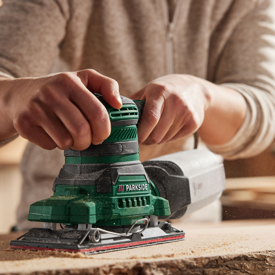 Close-up of hands using an electric sander on a wooden surface.
