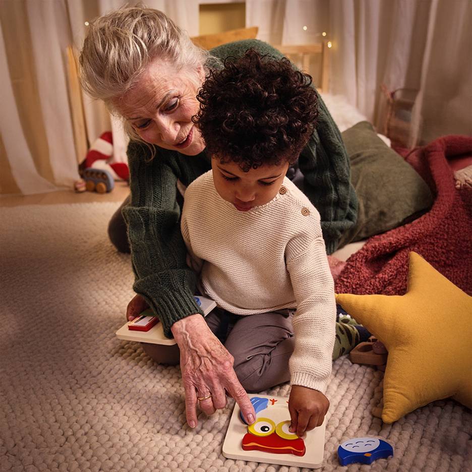 Grandmother and child playing with a wooden puzzle on a rug.
