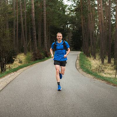 Man jogging in forest wearing athletic gear.