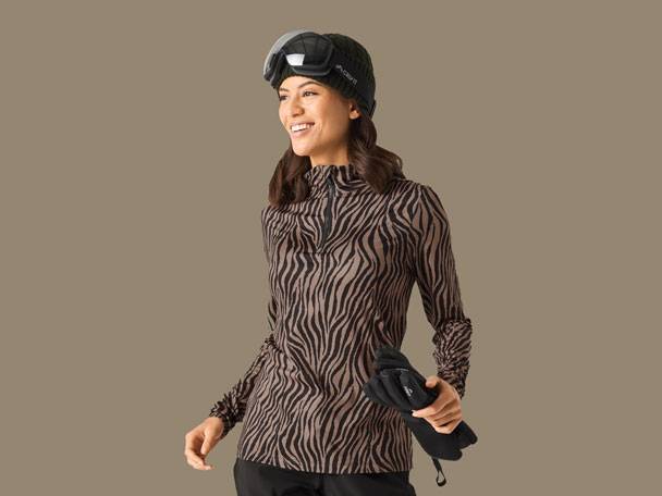 Woman in zebra print ski top, black ski hat, goggles, and gloves.