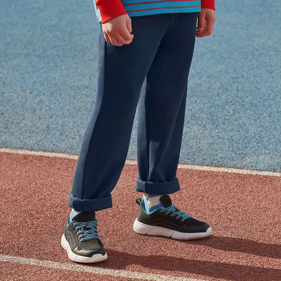 Navy sweatpants and black sneakers with blue laces on a running track.