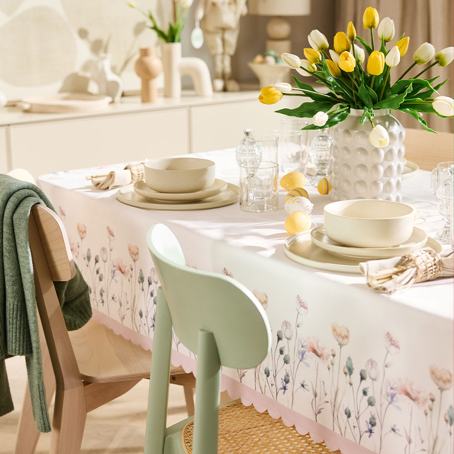 Easter table set with a floral tablecloth, ceramic dinnerware, and yellow and white tulips.