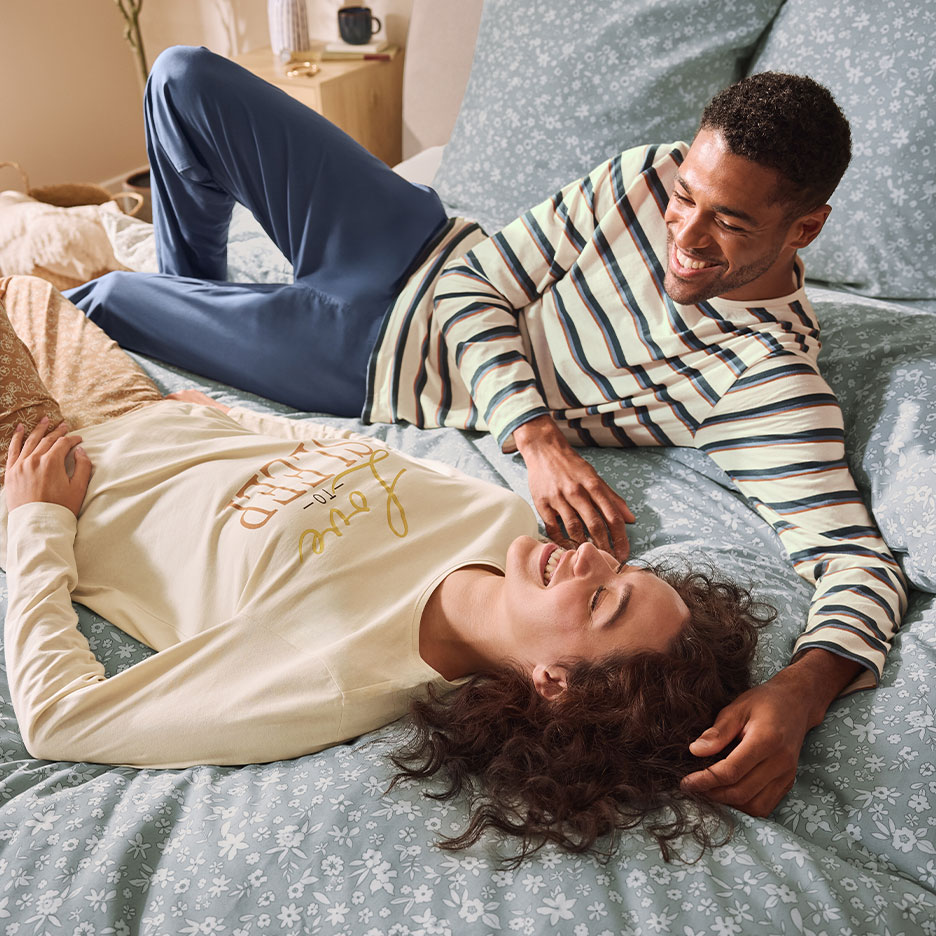 Couple in matching pajamas laughing in bed with floral bedding.