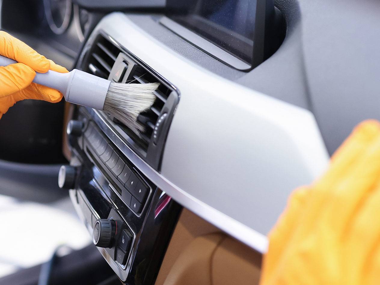 Cleaning a car interior with a detailing brush and rubber gloves.