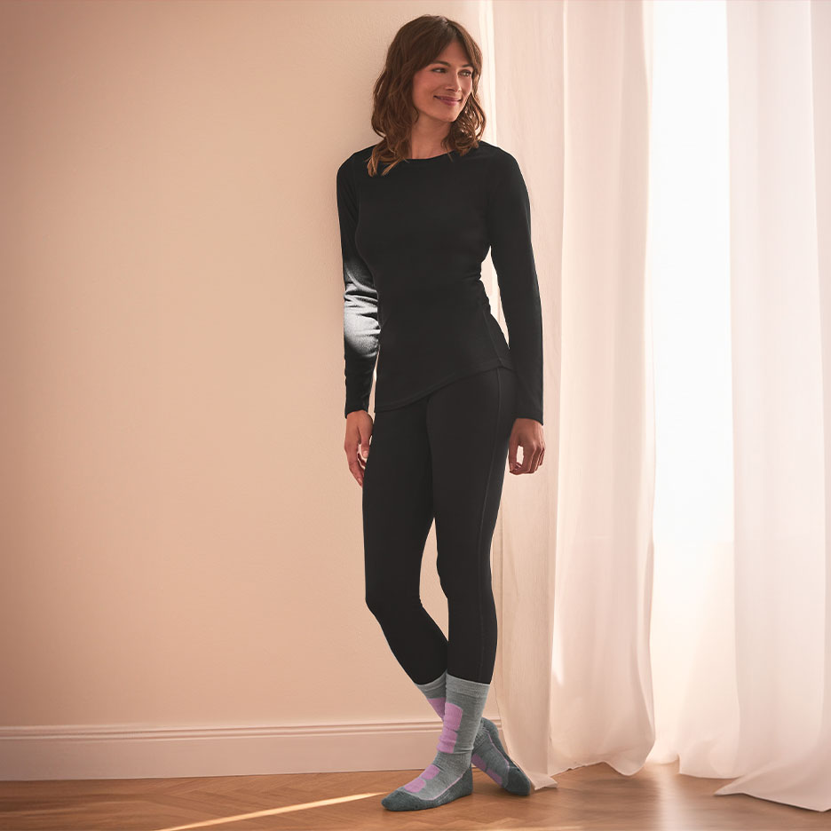 Woman in black thermal underwear and colorful socks, leaning against a wall.
