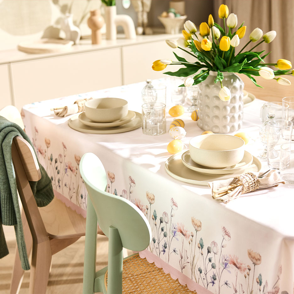 Easter table with a floral tablecloth, yellow tulips, and dinnerware in natural colors.
