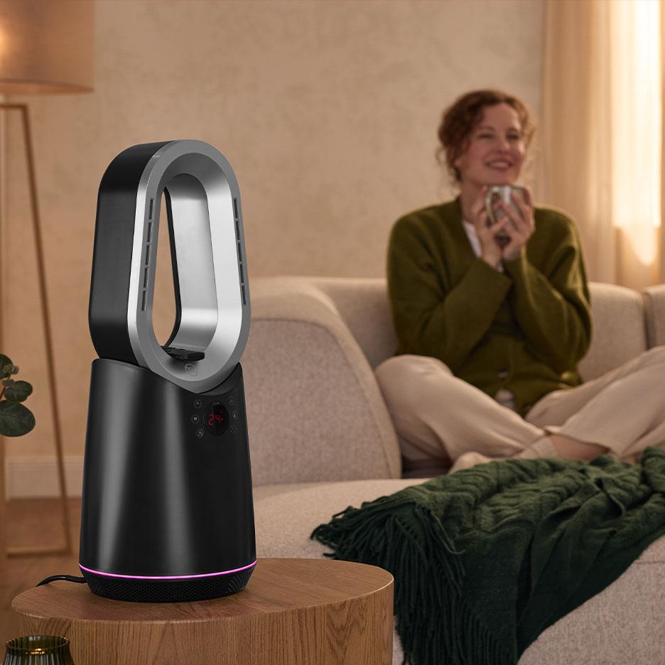Bladeless heater fan on a side table in a cozy living room with a woman on the sofa.