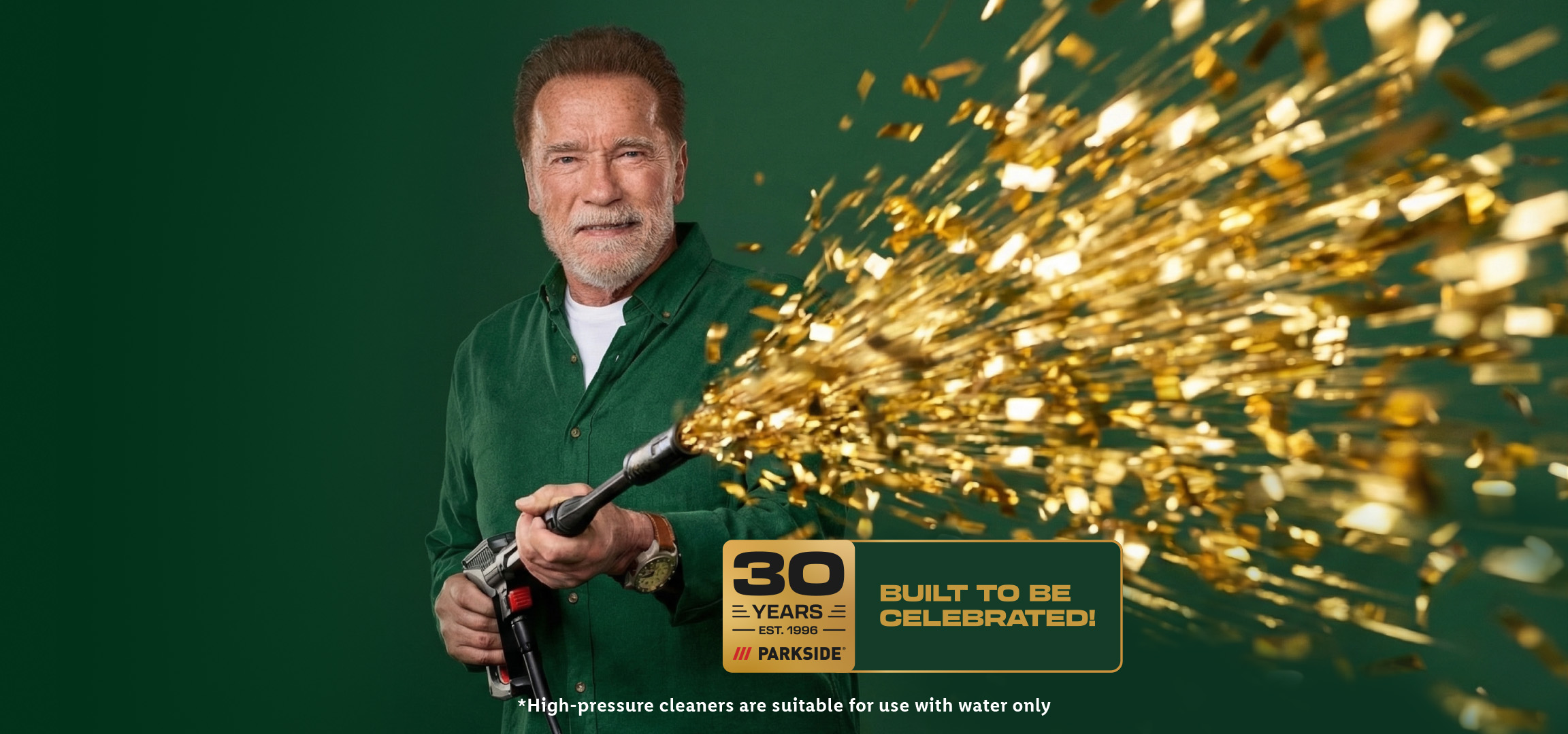 Man in green shirt holding a pressure cleaner spraying golden confetti, celebrating 30 years.