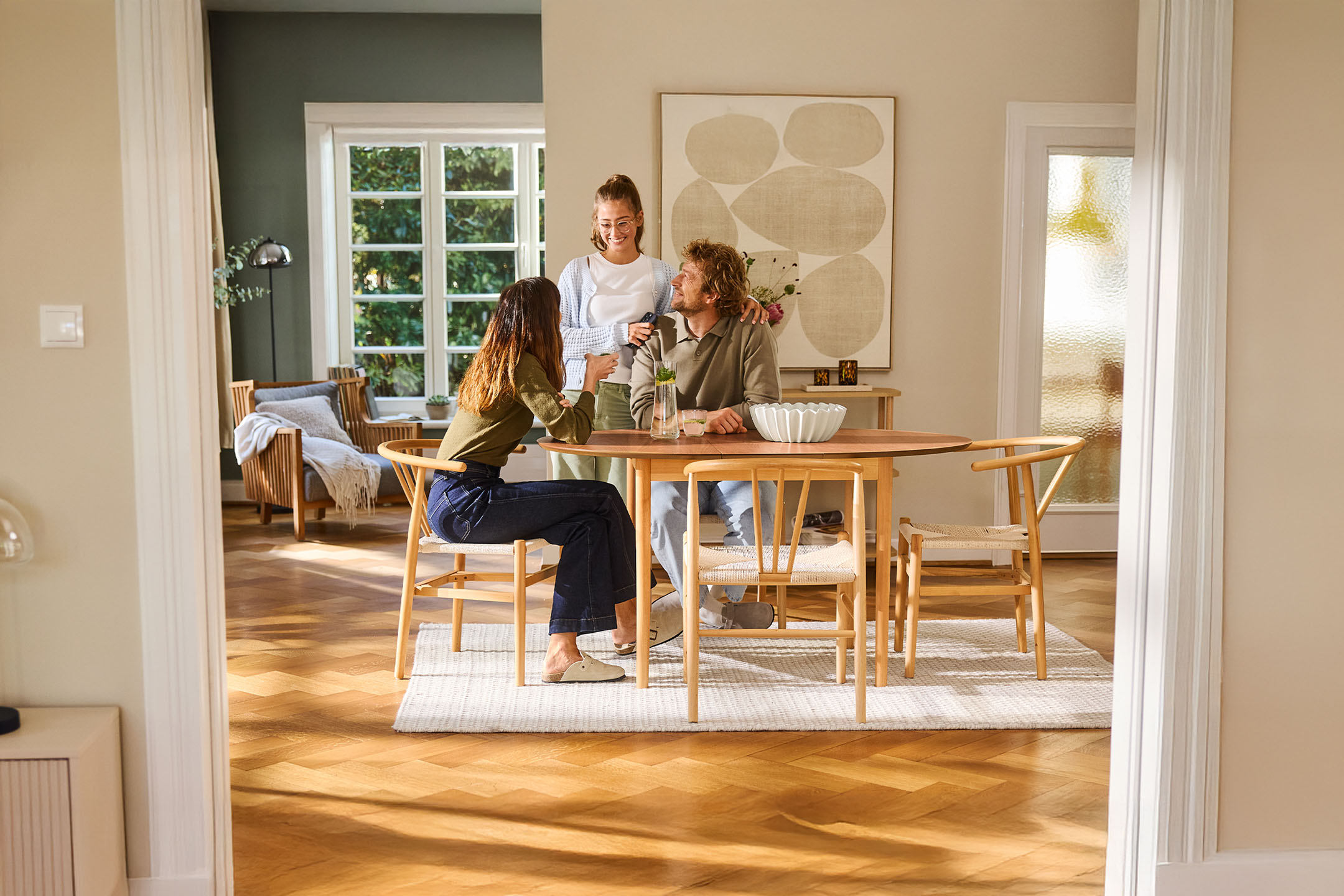 Three people at a wooden dining table with chairs, placed on a light-colored rug.