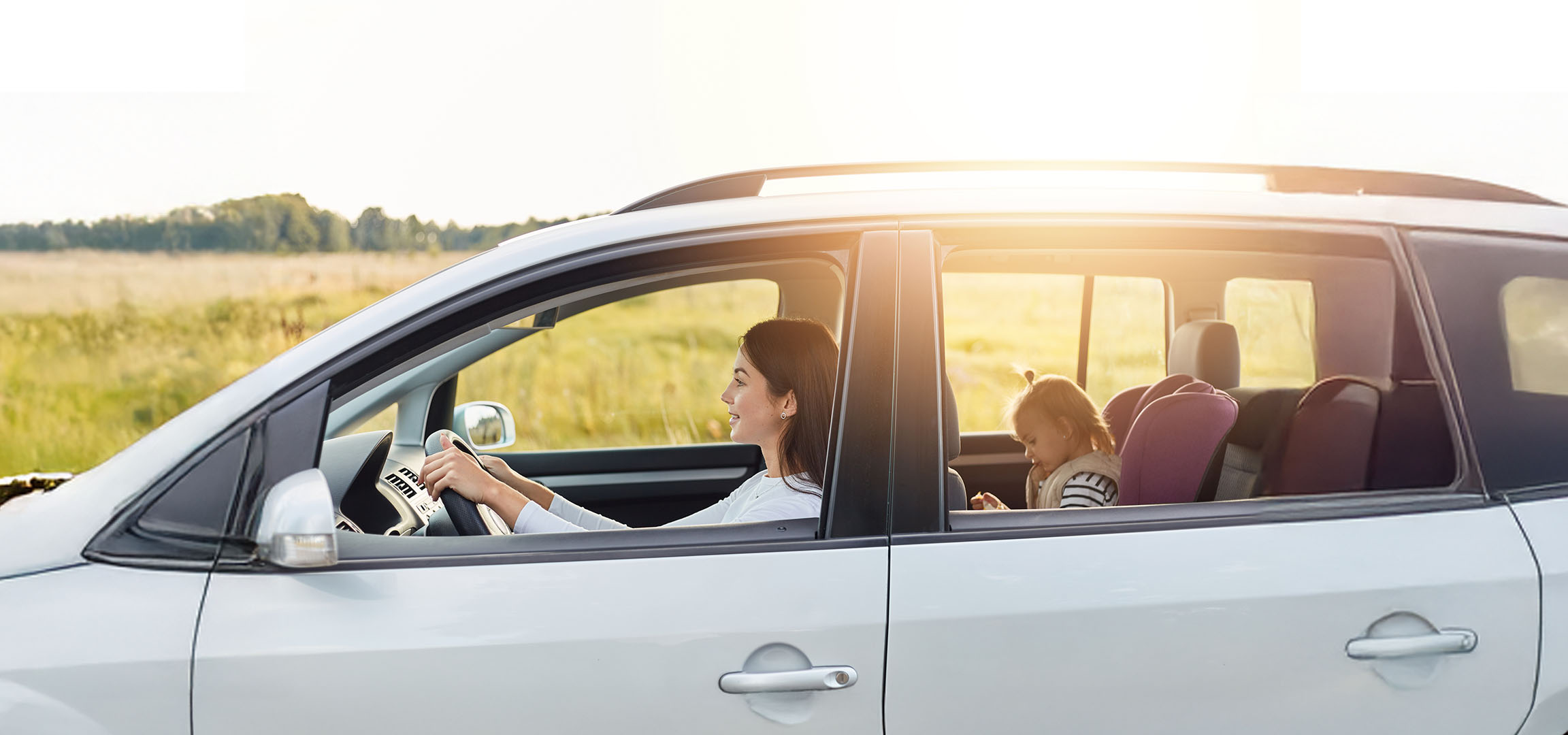 A woman drives a car with her daughter in the back seat.