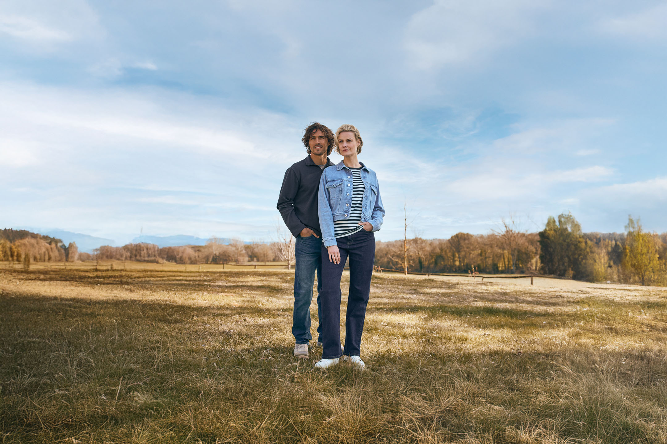 Couple in denim jackets in a rural setting.