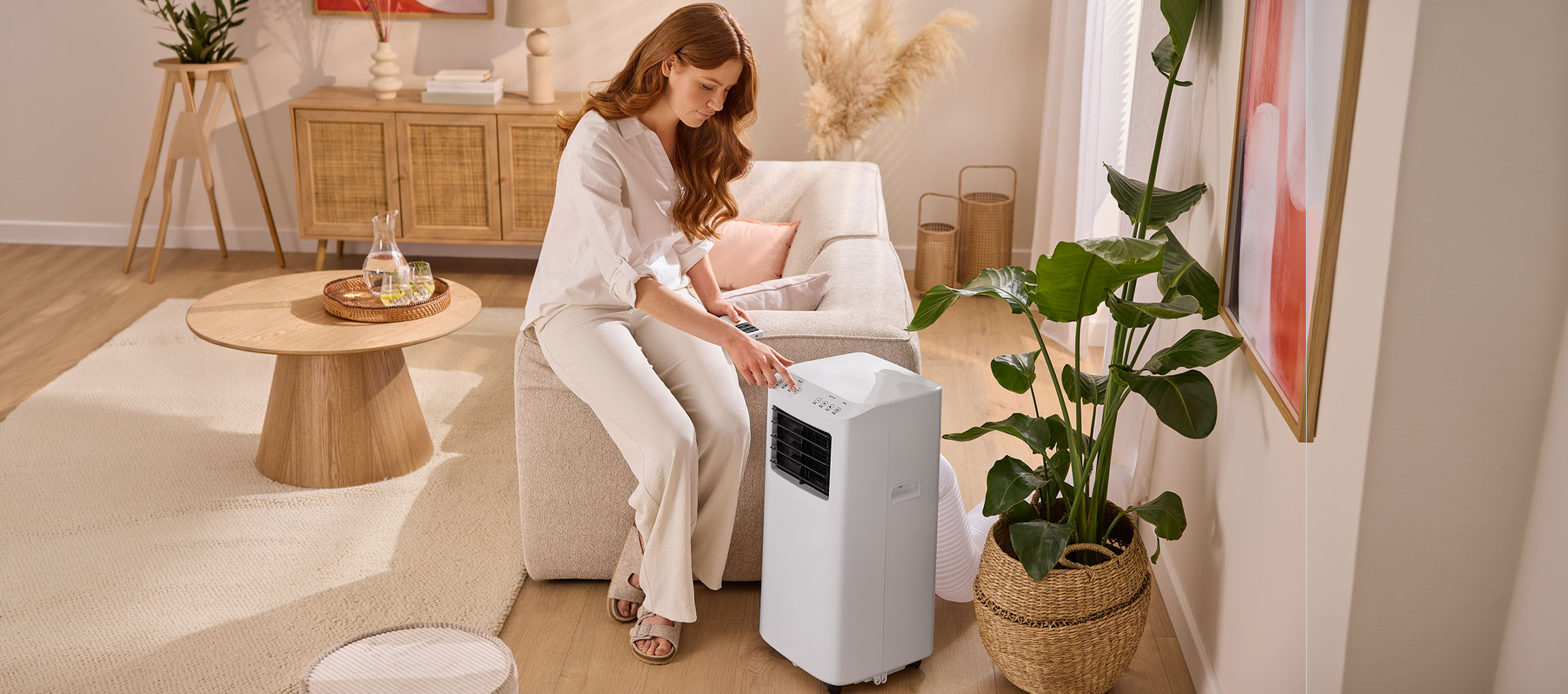 Woman adjusting a portable air conditioner in a living room with a sofa and coffee table.