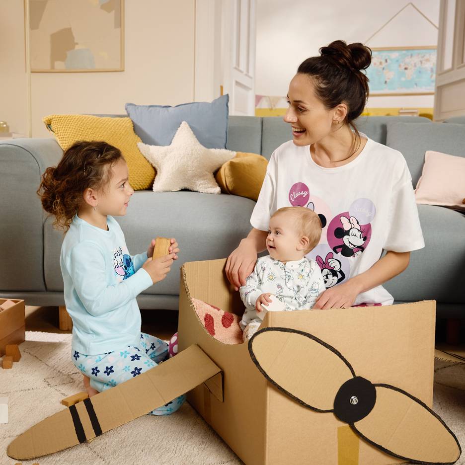 Mom and children playing with a cardboard box, with mom wearing a cartoon character t-shirt.